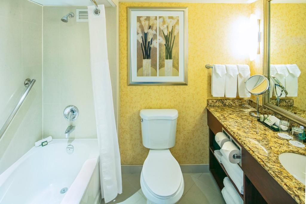 Badkamer van The Prince George Hotel, Halifax met bad, toilet en granieten wastafelblad naast een verlichte spiegel.