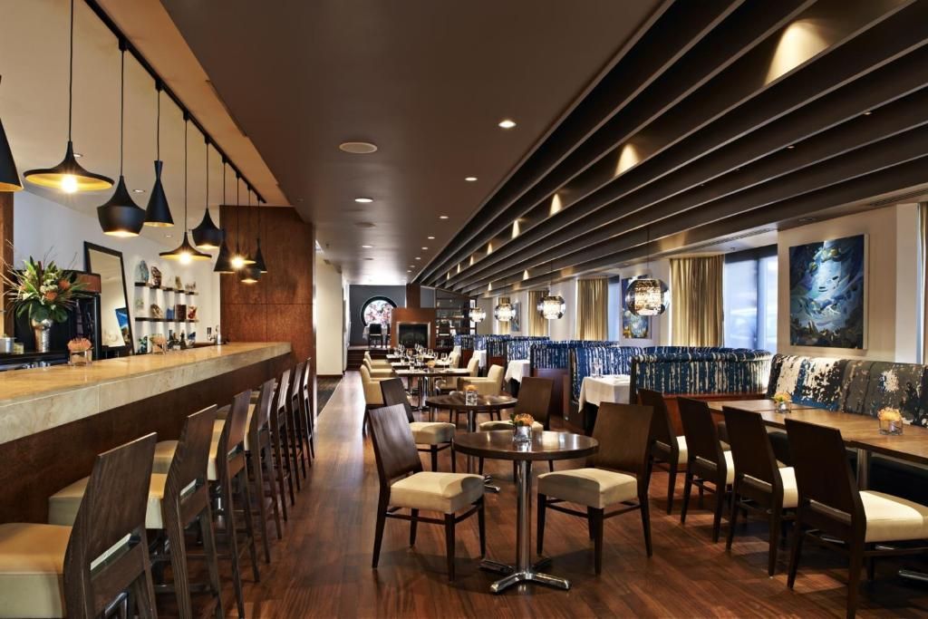 De sfeervol verlichte, moderne bar en lounge van The Prince George Hotel, Halifax met houten tafels, barkrukken en wanddecoratie in een ruim restaurantinterieur.
