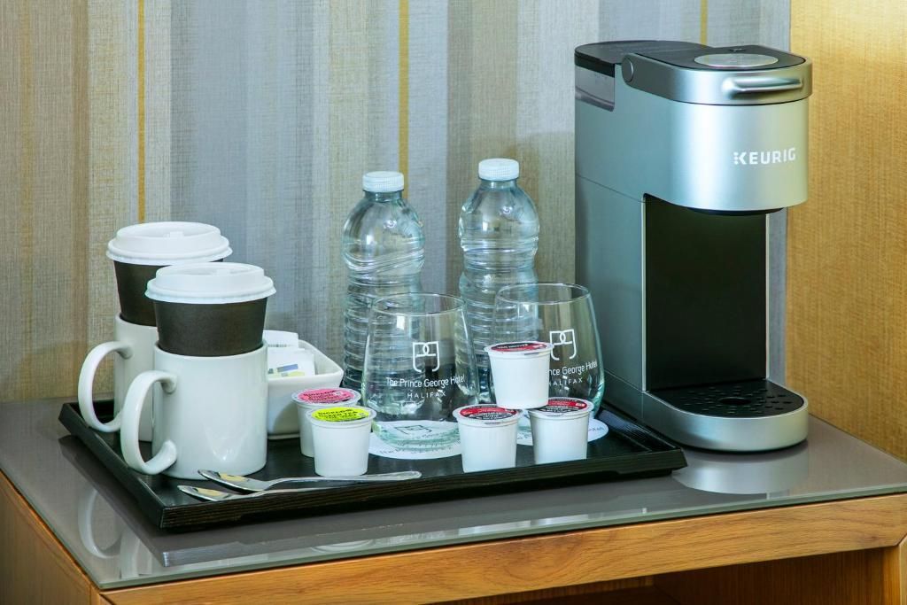 Een dienblad met koffie en water, kopjes, flessen water en een zilverkleurig koffiezetapparaat op een tafelblad van The Prince George Hotel, Halifax.