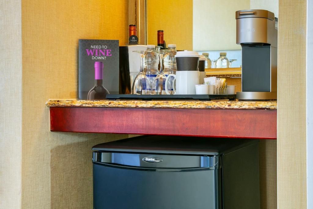 De minibar op de hotelkamer van The Prince George Hotel, Halifax bevat drankjes, een koffiezetapparaat en een minikoelkast onder een houten plank.