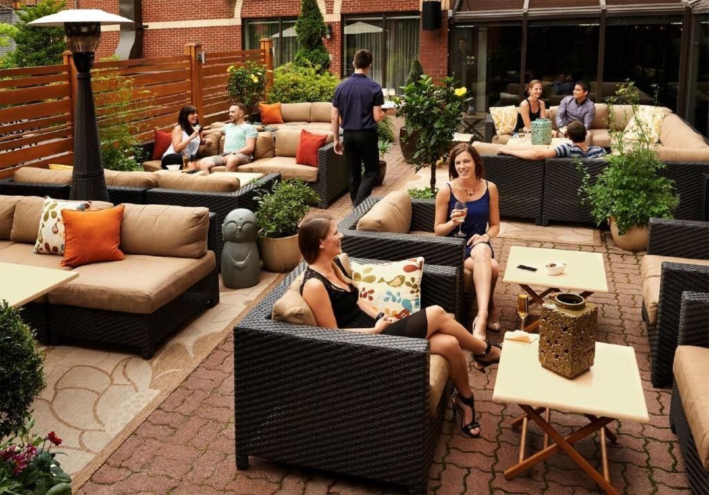 Mensen ontspannen op het terras van The Prince George Hotel, Halifax met rieten stoelen, tafels en bakstenen bestrating.