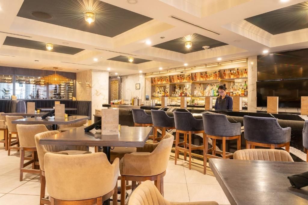 Moderne hotelloungebar met sfeervolle verlichting, tafels, stoelen en een barman achter de toonbank.
