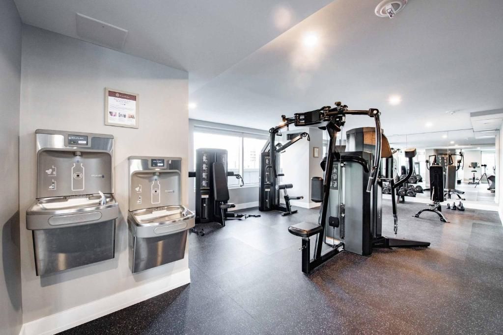 Lichte fitnessruimte met cardio- en krachttrainingsapparaten, waterfonteinen en spiegelwanden.