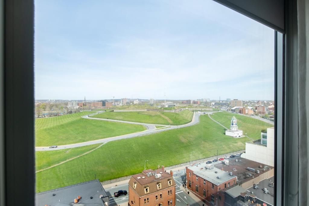 Uitzicht vanuit een raam op een groen park met kronkelende paden en stadsgebouwen in de verte.