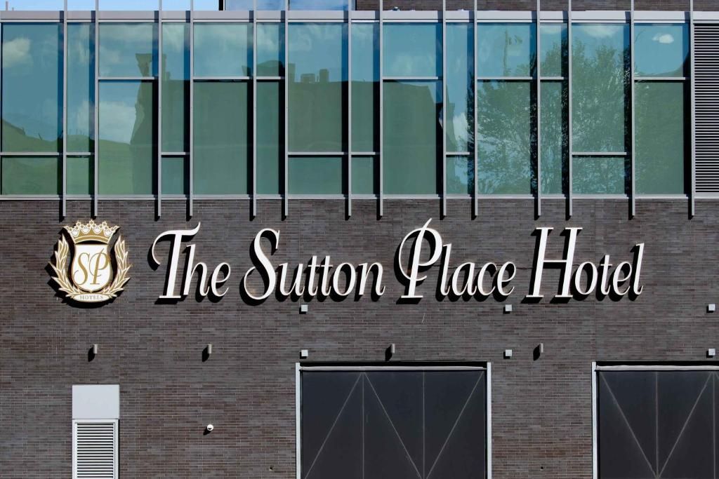 Het uithangbord van het Sutton Place Hotel op een bakstenen gebouw met blauw getinte ramen erboven.