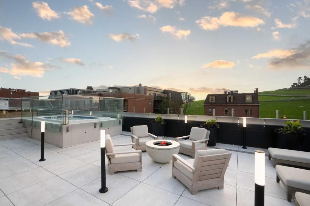 Modern dakterras met witte loungestoelen, vuurplaats, glazen balustrade en uitzicht over de stad bij zonsondergang.
