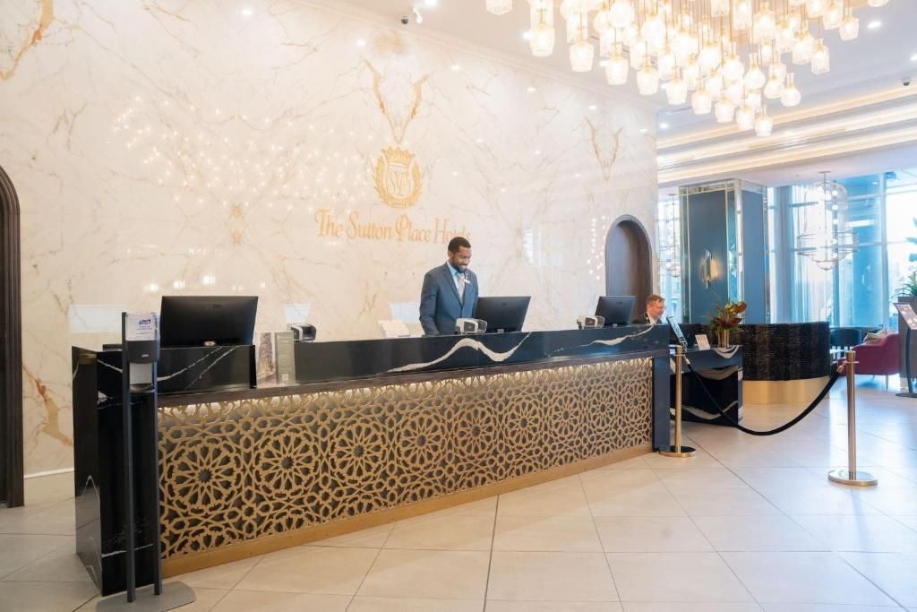 De receptie van een hotel staat bemand door een medewerker in een lichte, rijkversierde lobby.