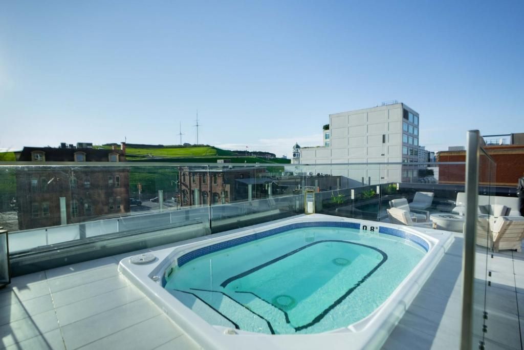 Zwembad op het dak met turquoise water, glazen balustrade en stedelijke gebouwen op de achtergrond.