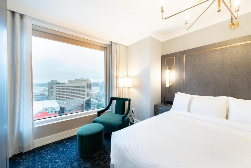 Moderne hotelkamer met kingsize bed, turquoise stoel, groot raam en uitzicht op de stad.