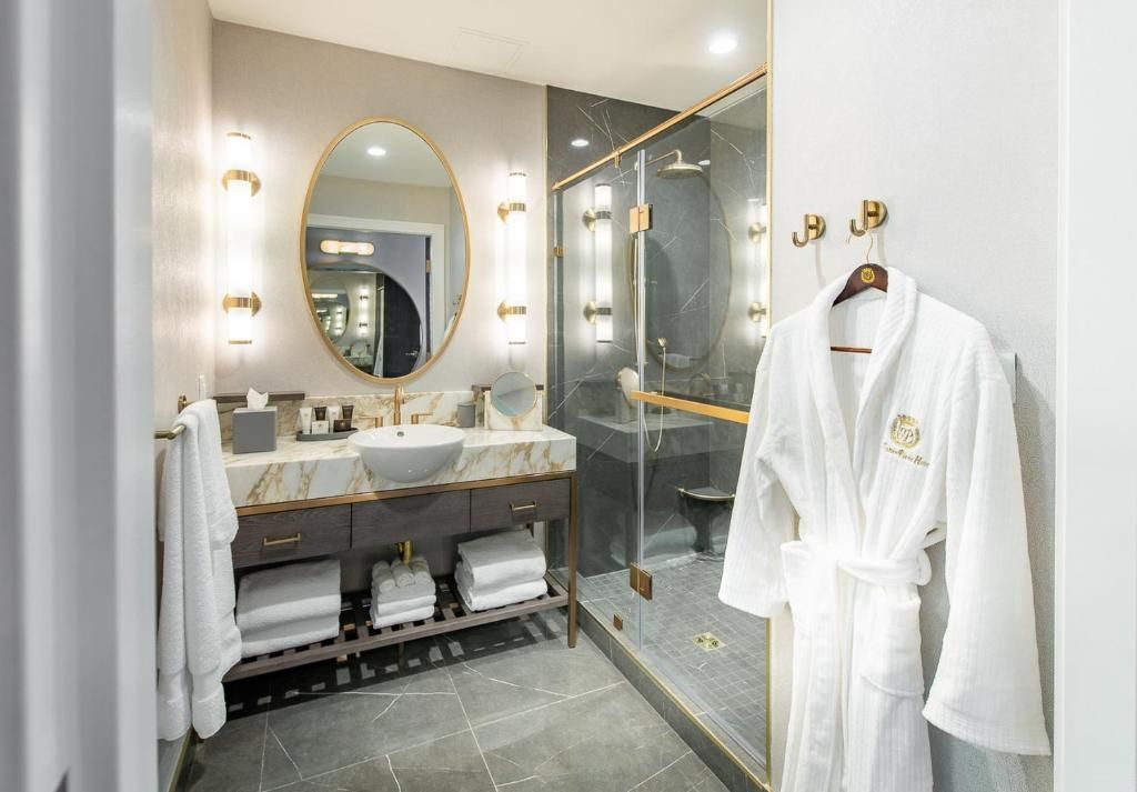 Luxe badkamer met dubbele wastafel, ovale spiegel, glazen douchecabine en witte badjas aan een haak.