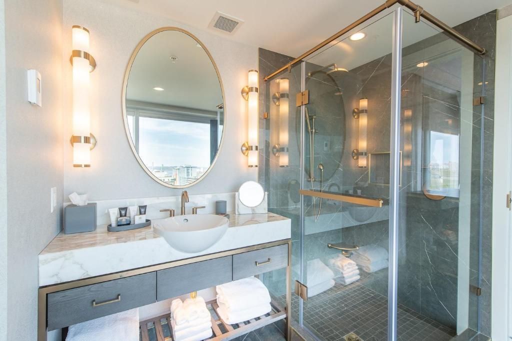 Lichte, moderne badkamer met dubbele wastafel, ovale spiegel, wandlampen en glazen douchecabine.