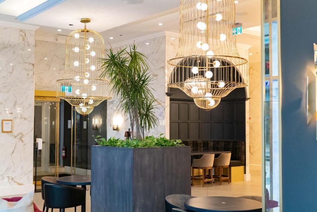 Elegante hotellobby met kroonluchters, donker meubilair en een hoge kamerplant als centraal element.