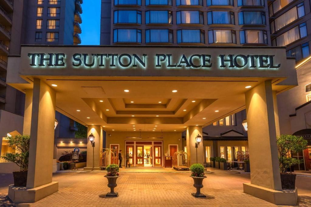 De ingang van het Sutton Place Hotel bij schemering, met een warm verlichte lobby en grote zuilen met baldakijnen.