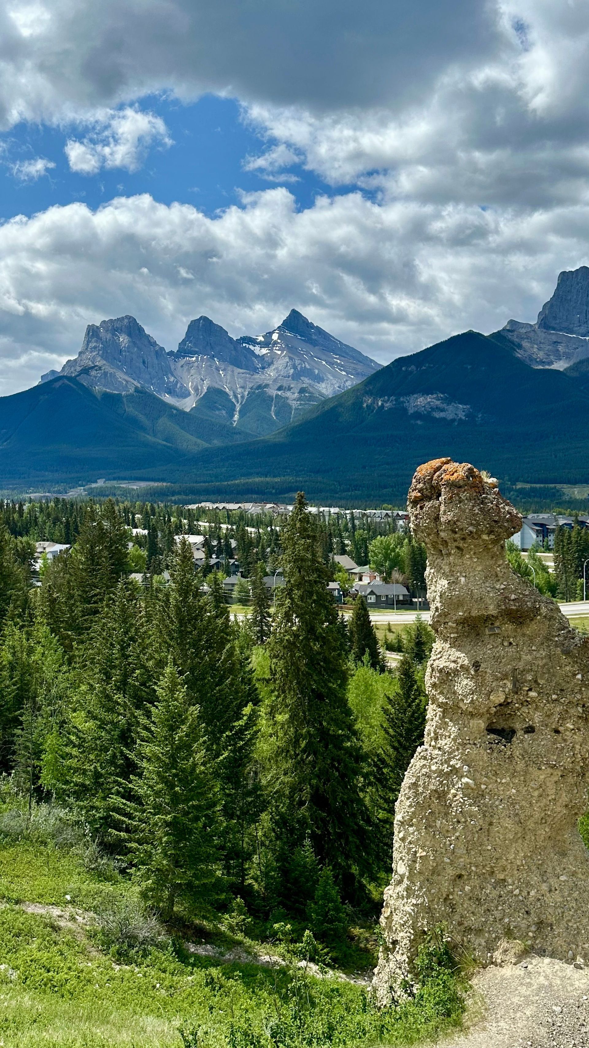 Bergtoppen boven een groen bos nabij Banff, met een stenen ruïne op de voorgrond onder een bewolkte blauwe hemel.