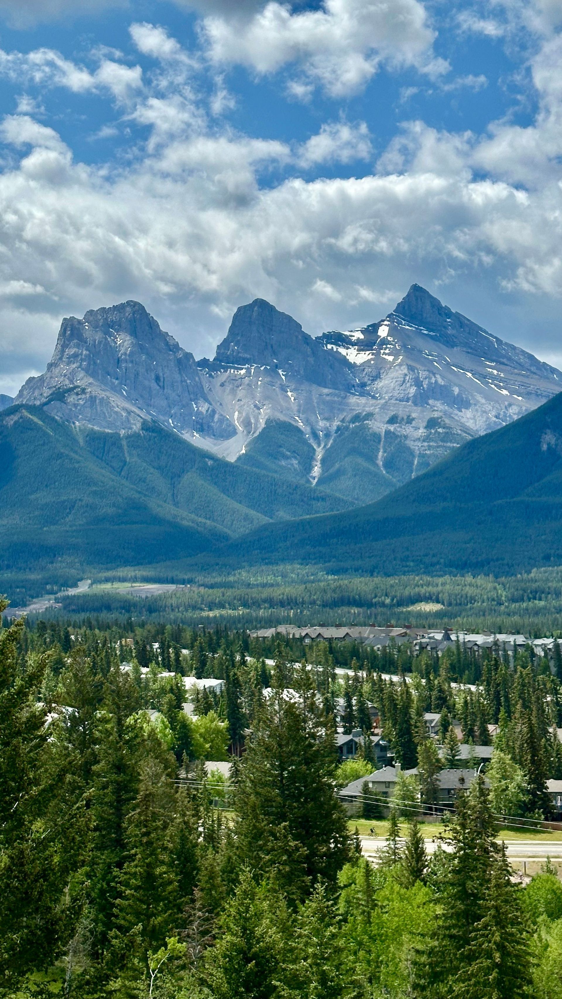 Bergtoppen nabij Banff boven een groene vallei onder een blauwe hemel met verspreide wolken.