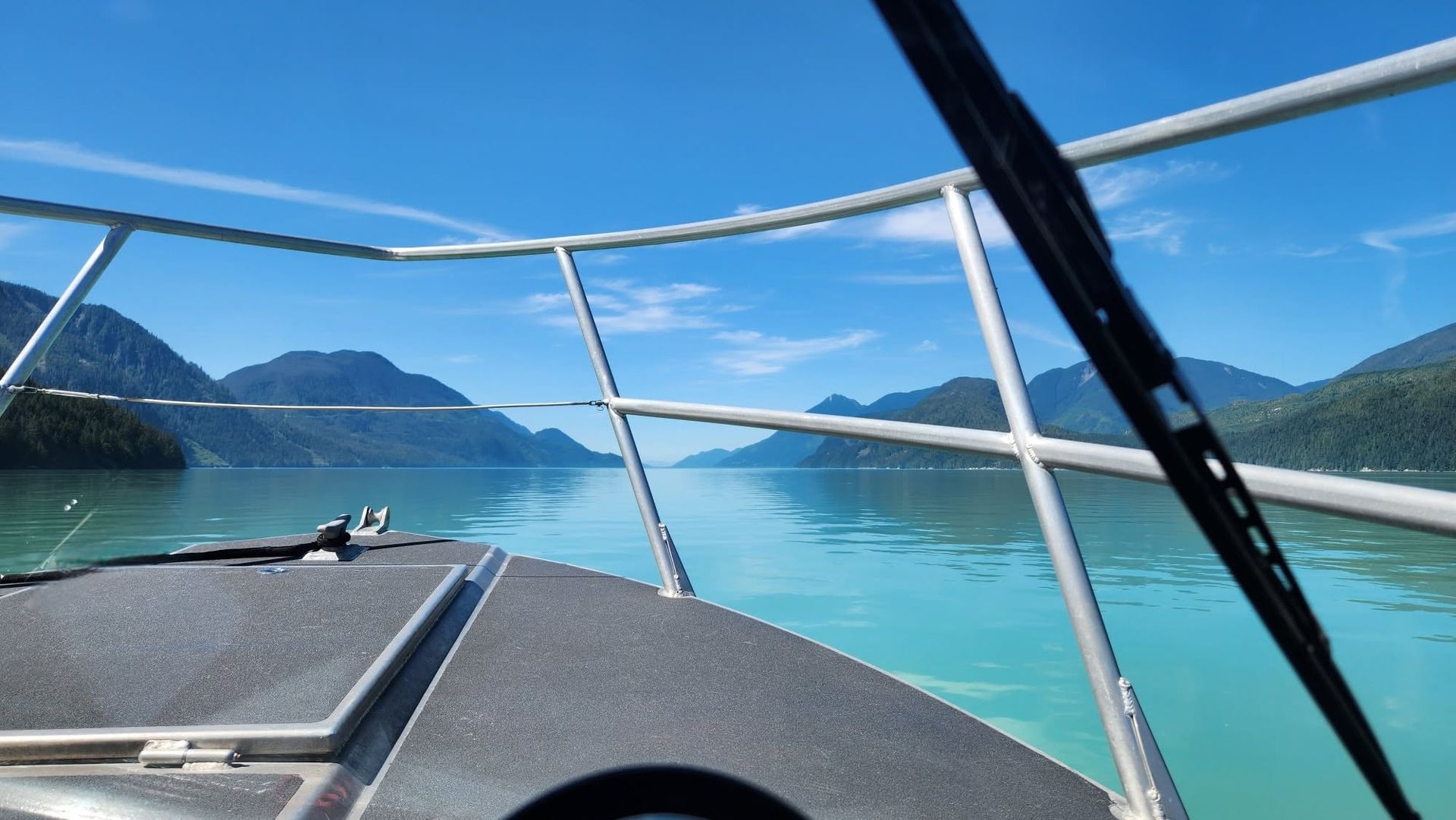 Uitzicht vanaf een boot in Canada over turkooizen water richting beboste eilanden en verre bergen onder een heldere hemel.