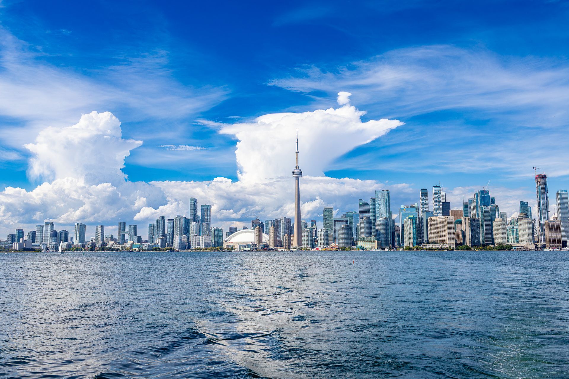 De skyline van Toronto met de CN Tower aan de overkant van het water, onder een helderblauwe hemel.