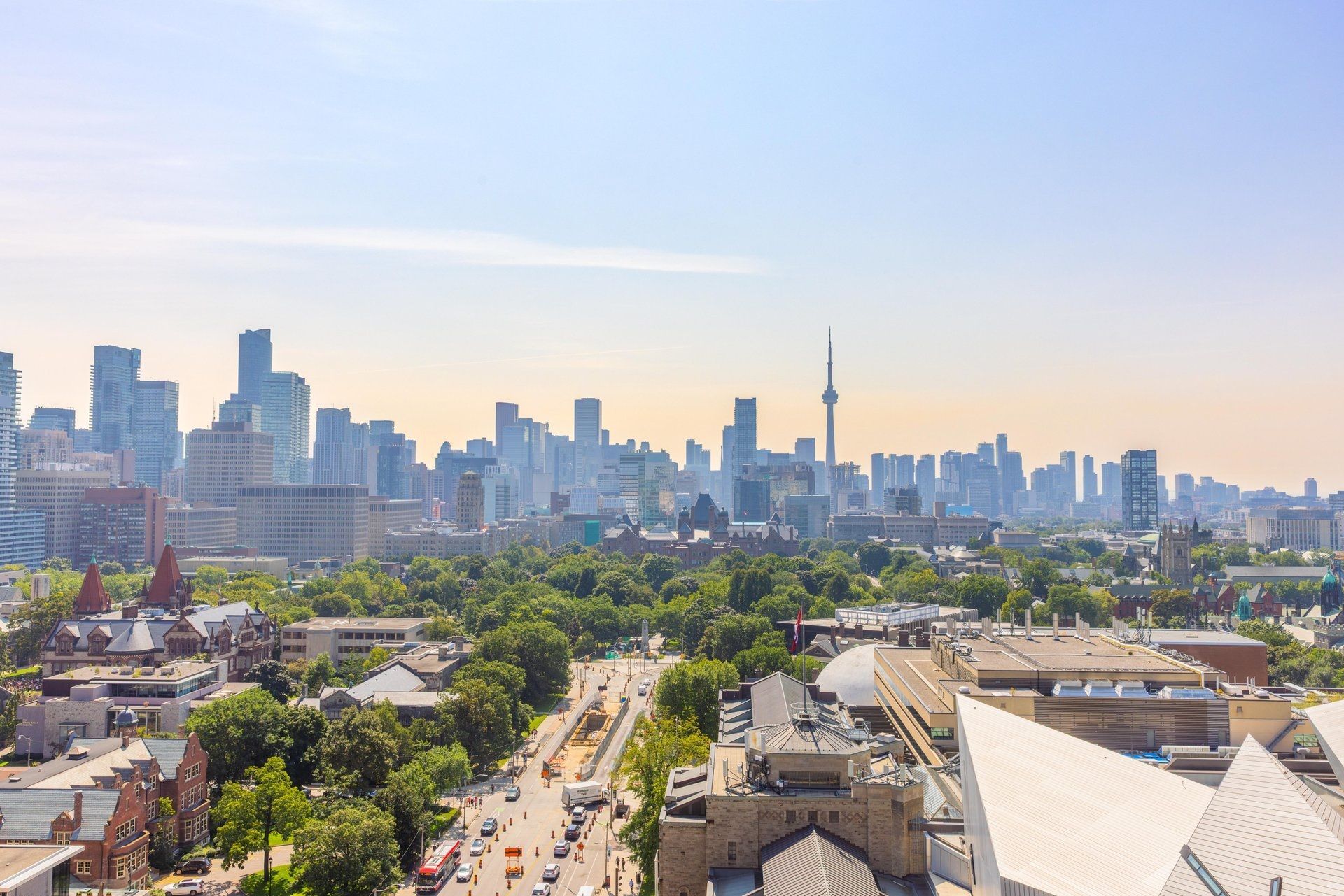 De skyline van de stad Toronto  bij zonsondergang, boven een met bomen omzoomde boulevard en laagbouw.