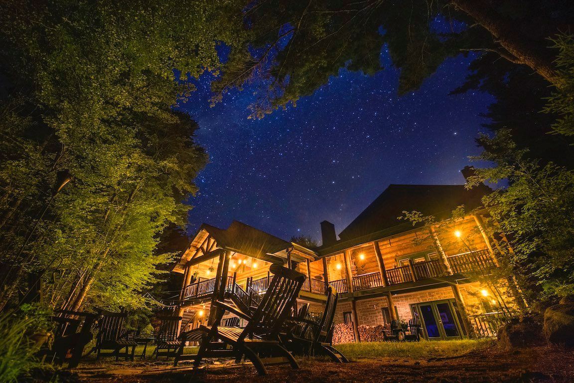 Verlichte lodgegebouwen gloeien warm onder een sterrenhemel, omlijst door bomen.