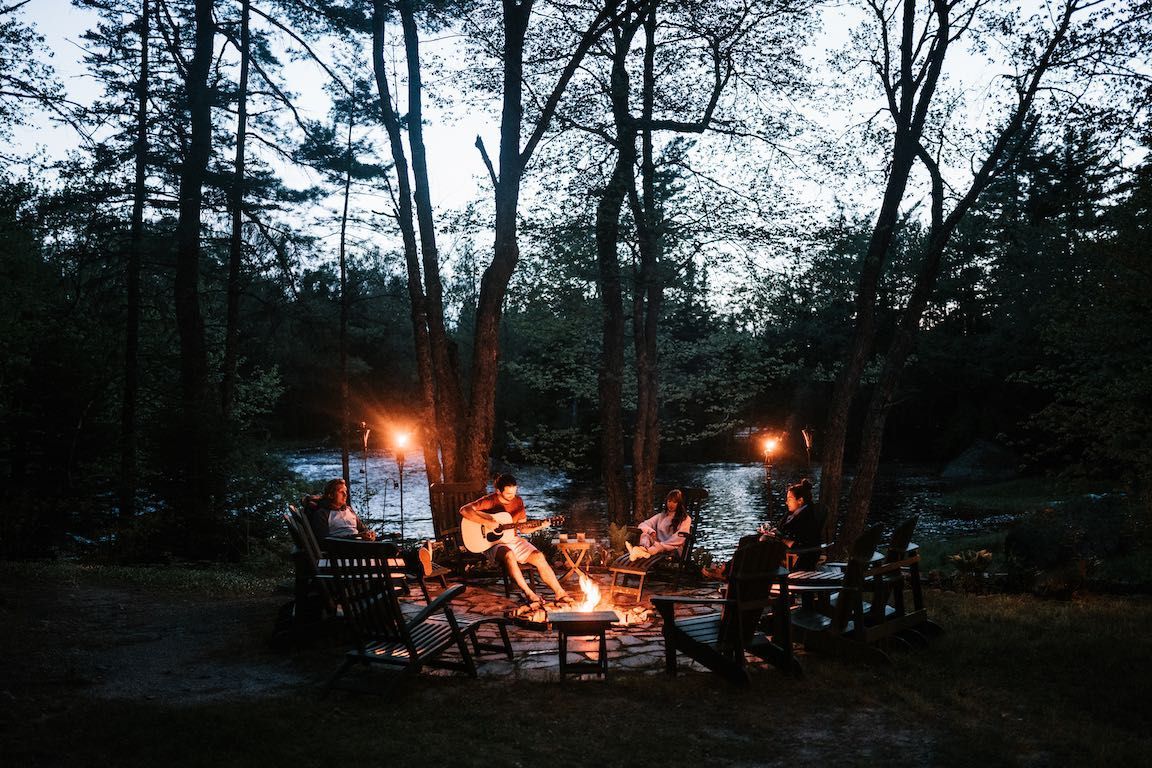 Mensen hadden zich verzameld rond een gloeiend kampvuur op een donkere open plek in het bos, in de schemering.