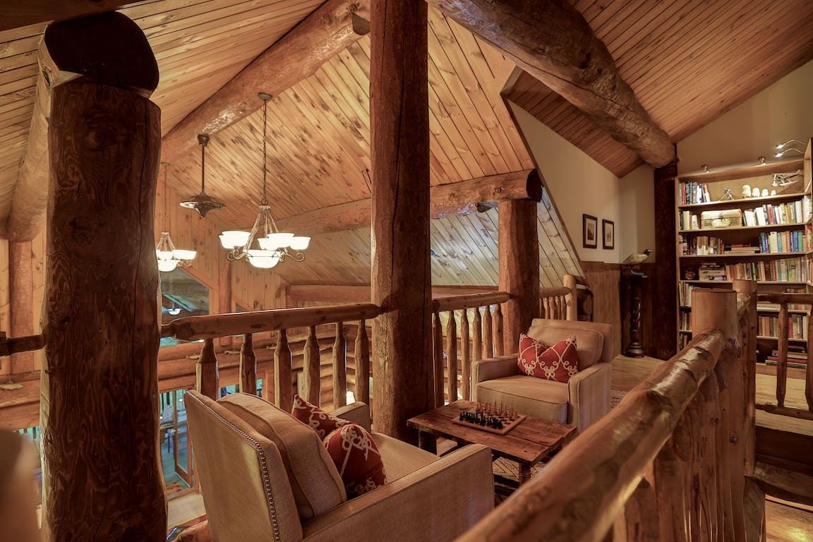 Houten loftlounge met gewelfd plafond, balustrade, fauteuils en warme sfeerverlichting.