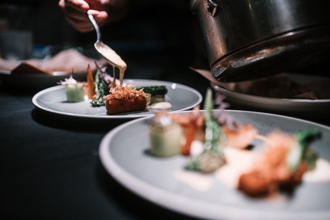 De chef-kok schikt gastronomische hapjes op witte borden in een schemerig verlichte restaurantkeuken.