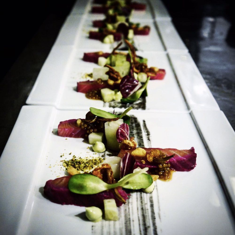 Een gastronomisch gerecht, gegarneerd met rode, groene en gouden accenten, geserveerd op een langwerpig wit bord.