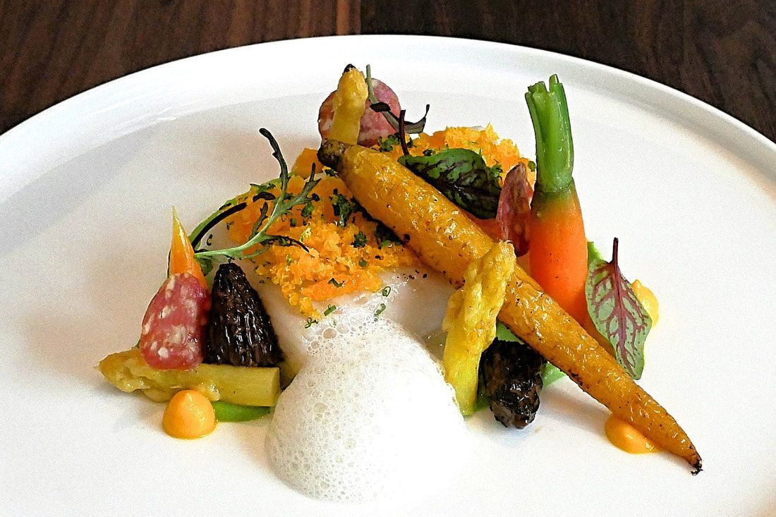 Een gastronomisch groentegerecht met asperges, wortelen en rijst, geserveerd op een wit bord.