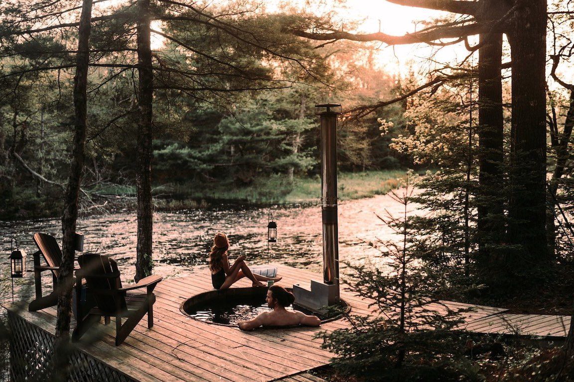Mensen ontspannen op een houten terras in een bos bij zonsondergang.