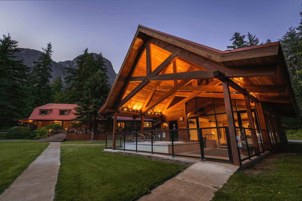 De wellness van Tweedsmuir Park Lodge met warm oranje licht in de schemering, naast een graspad en bomen.