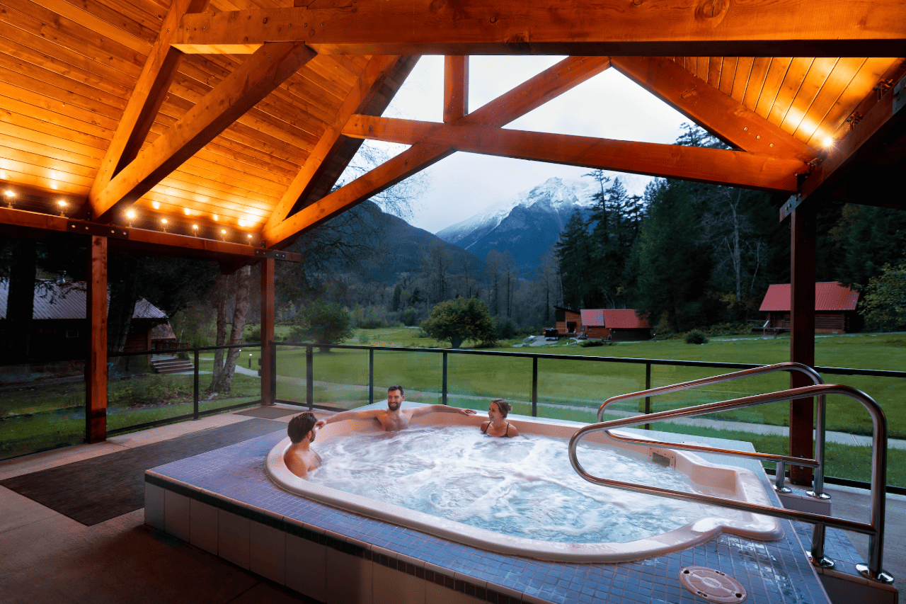 Buitenjacuzzi van Tweedsmuir Park Lodge onder een houten paviljoen met uitzicht op mistige bergen bij zonsondergang.