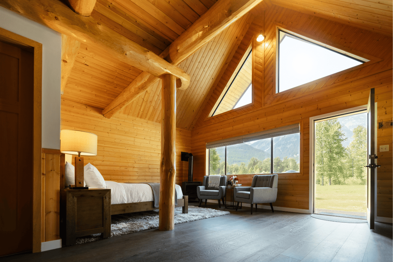 Een sfeervol houten interieur van Tweedsmuir Park Lodge met gewelfd plafond, bed, zithoek en een groot driehoekig raam met uitzicht op de bomen.
