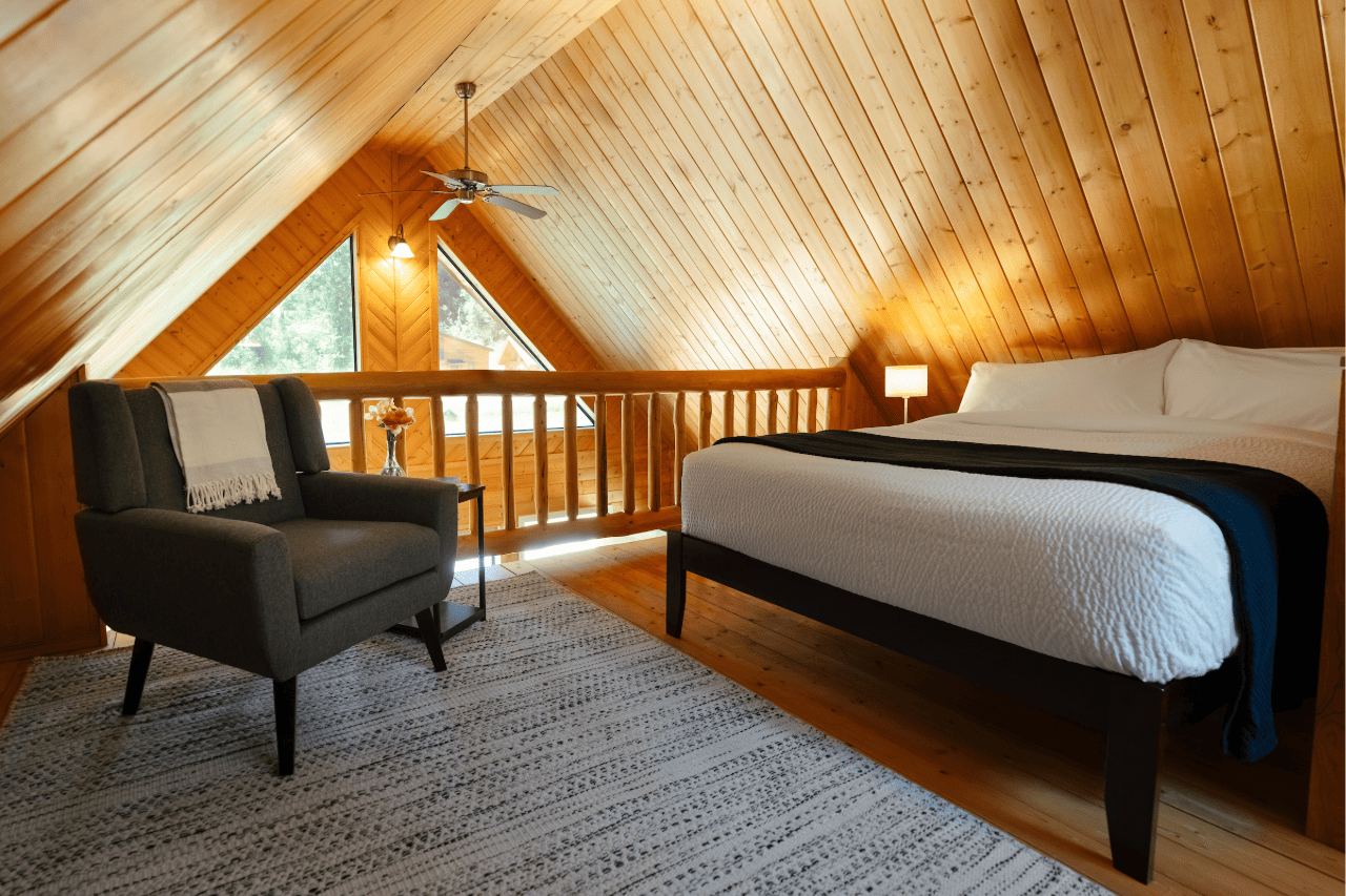 Gezellige slaapkamer op de vide van Tweedsmuir Park Lodge met schuin houten plafond, tweepersoonsbed, fauteuil en sfeervolle lampen.