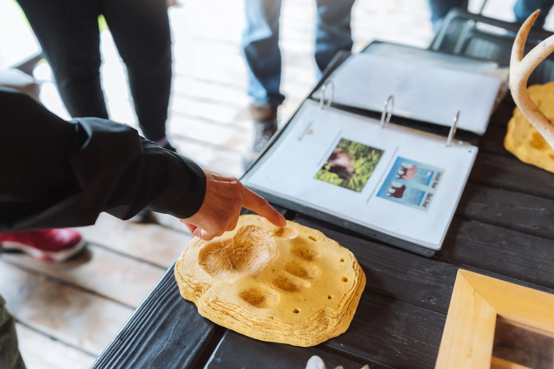 Iemand doopt een tortillachip in een kom naast een tablet op een houten tafel.