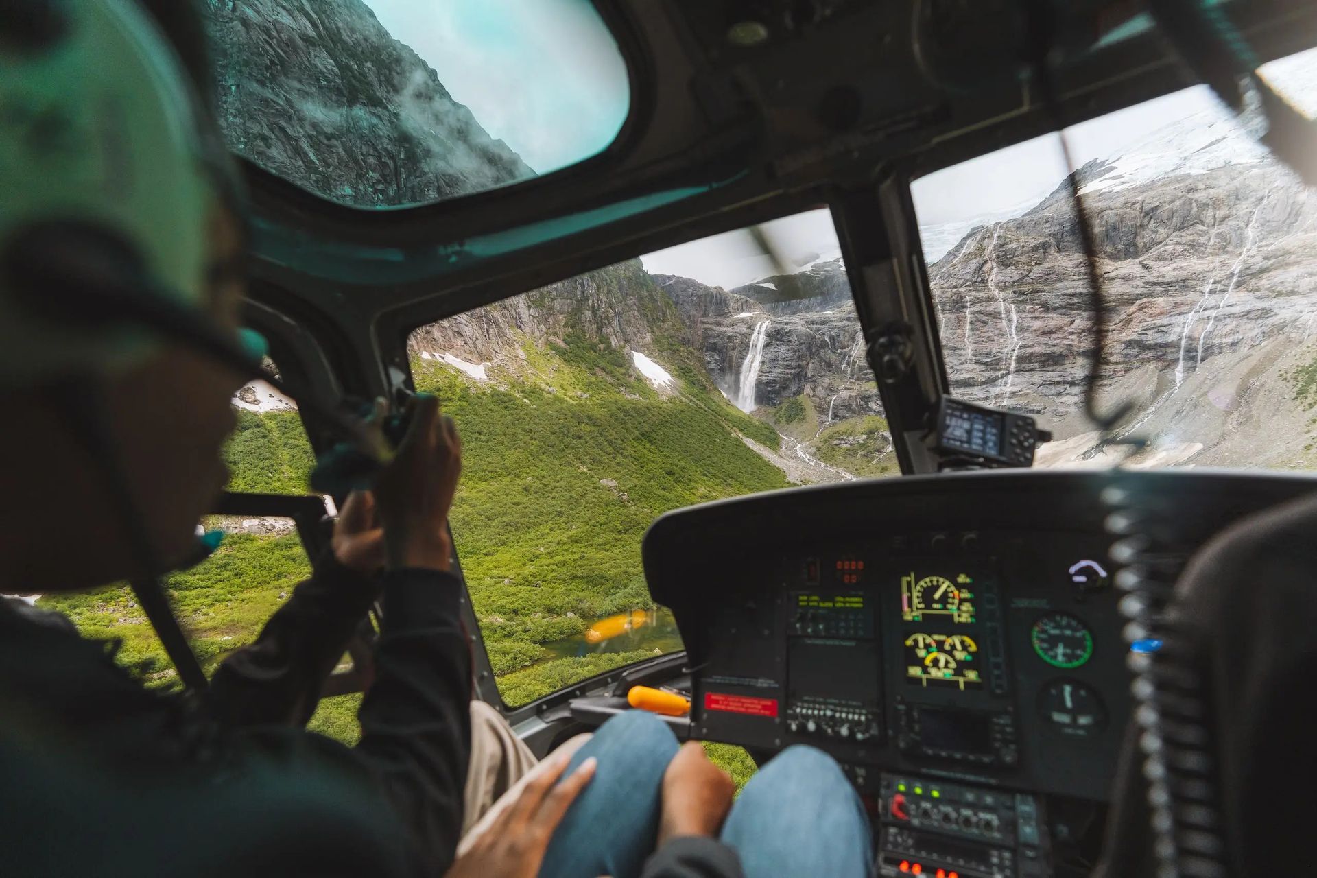 Helikoptercockpit tijdens een vlucht laag door een smalle kloof, piloot aan de stuurknuppel, verlicht dashboard.