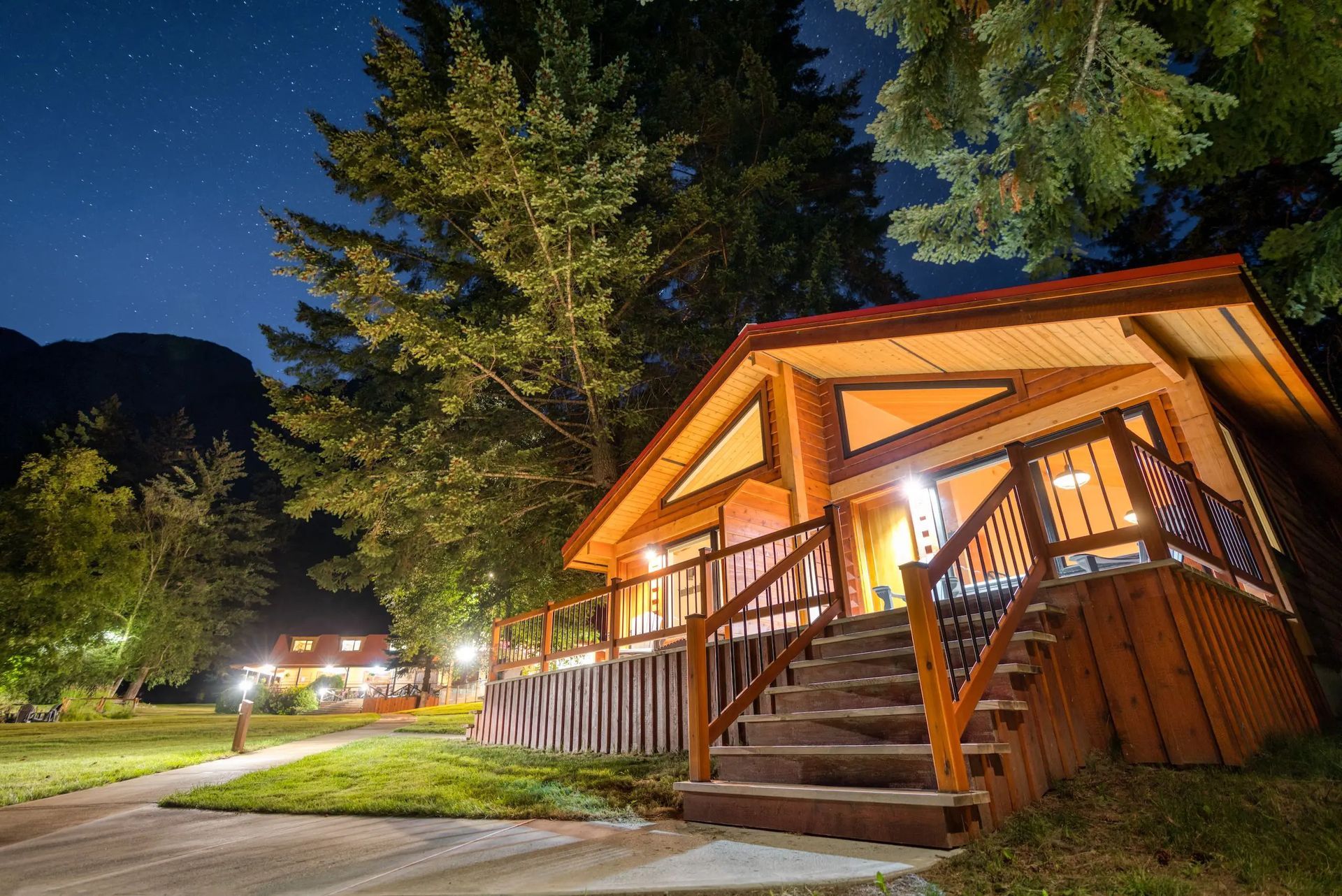 Een verlichte blokhut van Tweedsmuir Park Lodge met verandaverlichting 's nachts, omgeven door bomen onder een sterrenhemel.