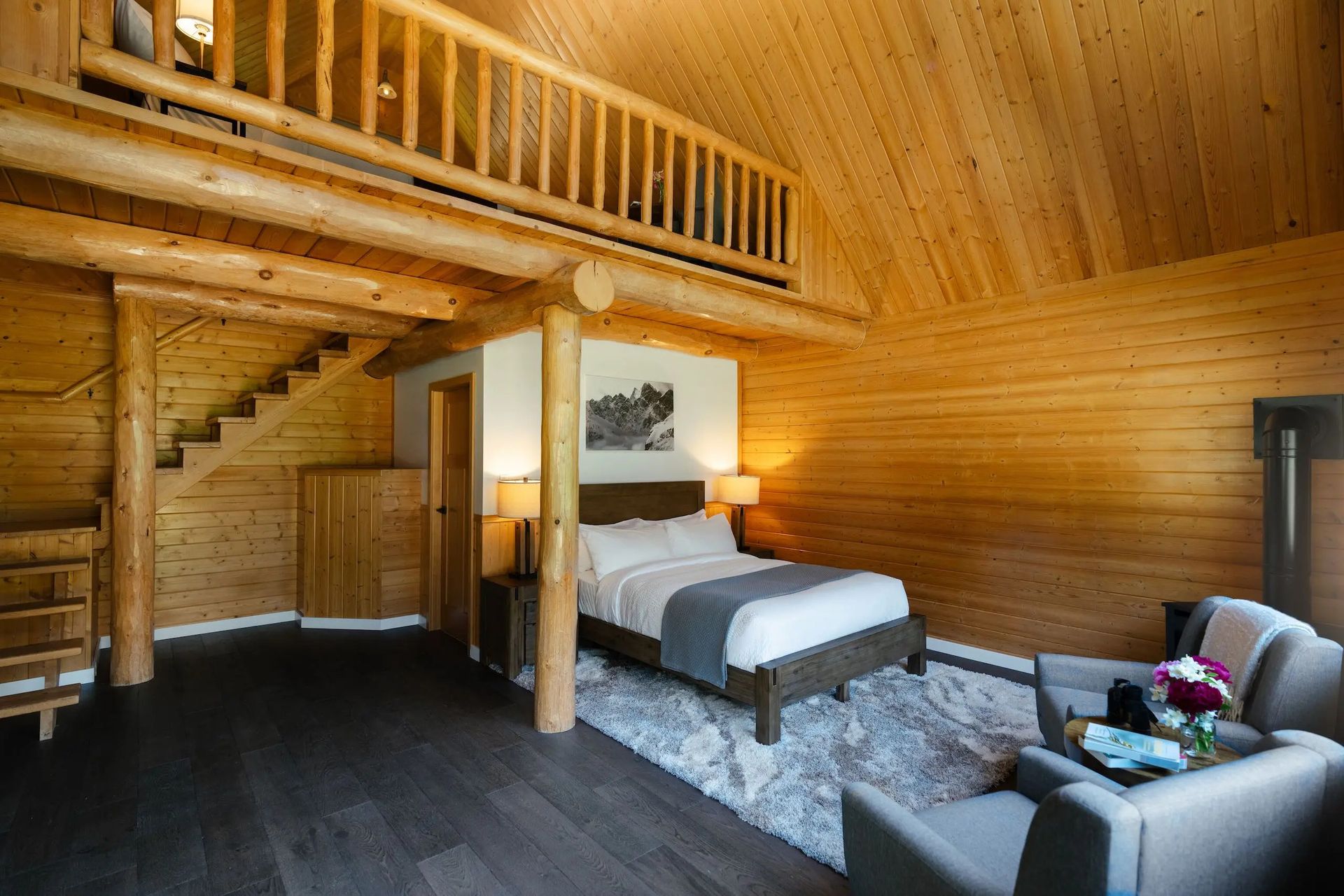 Rustieke slaapkamer van Tweedsmuir Park Lodge op de vide met houten lambrisering, een bed, een trap en een zithoekje naast een raam.