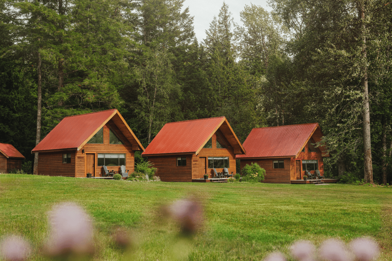 Drie kleine houten hutjes met rode daken van Tweedsmuir Park Lodge op een groene open plek in het bos.