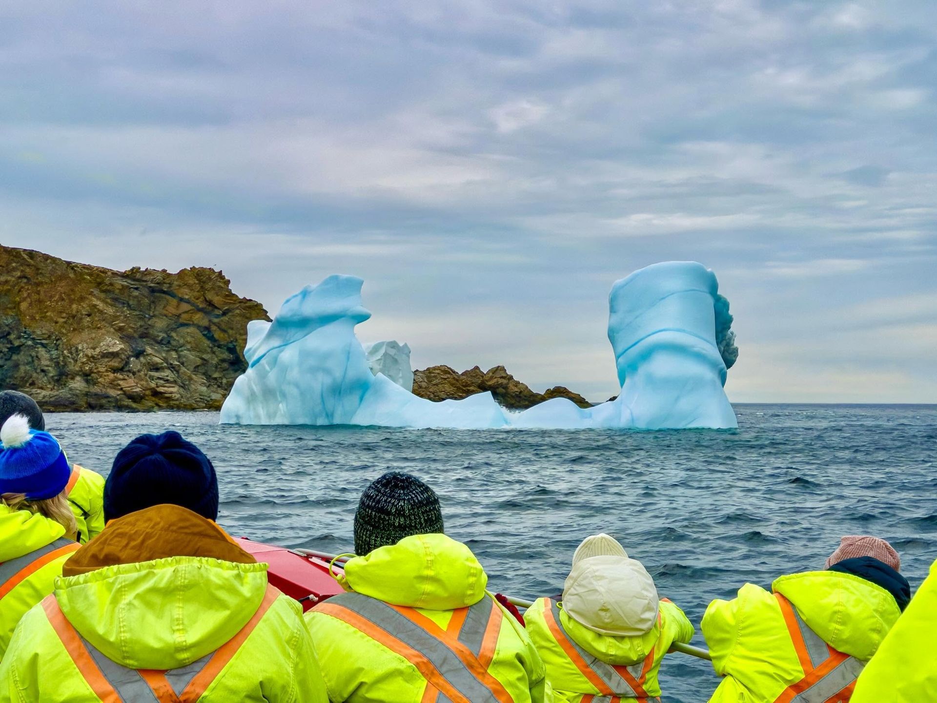 Mensen in felgekleurde jassen kijken naar ijsbergen die drijven in een koude oceaan onder een bewolkte hemel nabij Twillingate in Newfoundland, Canada.