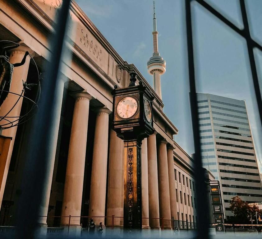 Historisch treinstation met klokkentoren en skyline, gezien door een raamkozijn bij zonsondergang.