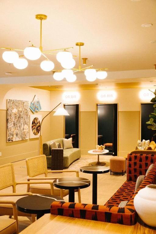 Moderne lounge met beige zitmeubelen, ronde tafels, warme hanglampen en abstracte muurdecoratie.