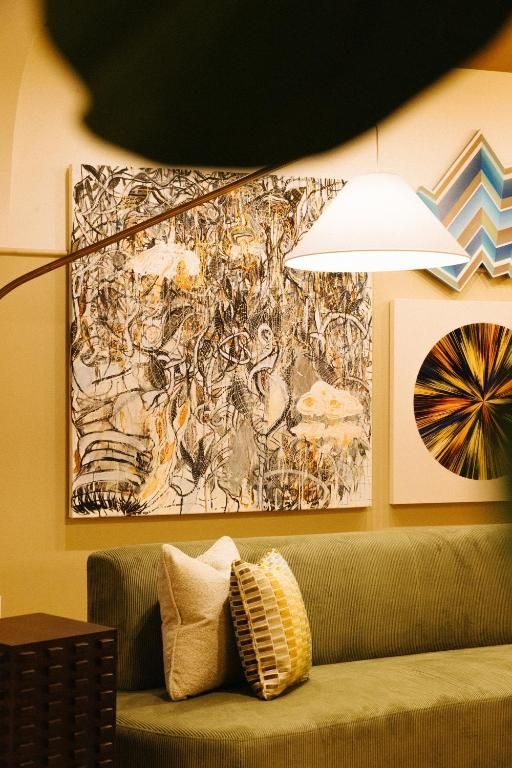 Gezellige woonkamer met olijfgroene bank, abstracte muurdecoratie, hanglamp en sierkussens.