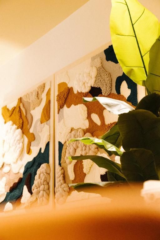 Zonovergoten wanddecoratie met abstracte bloemenpanelen naast een grote groene kamerplant.