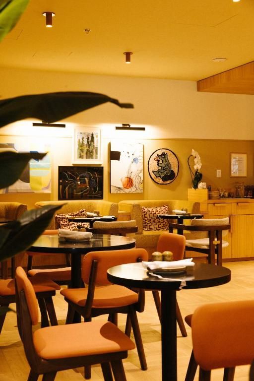 Lege lobby van een hotel met oranje stoelen, ronde tafels en warme gele verlichting.