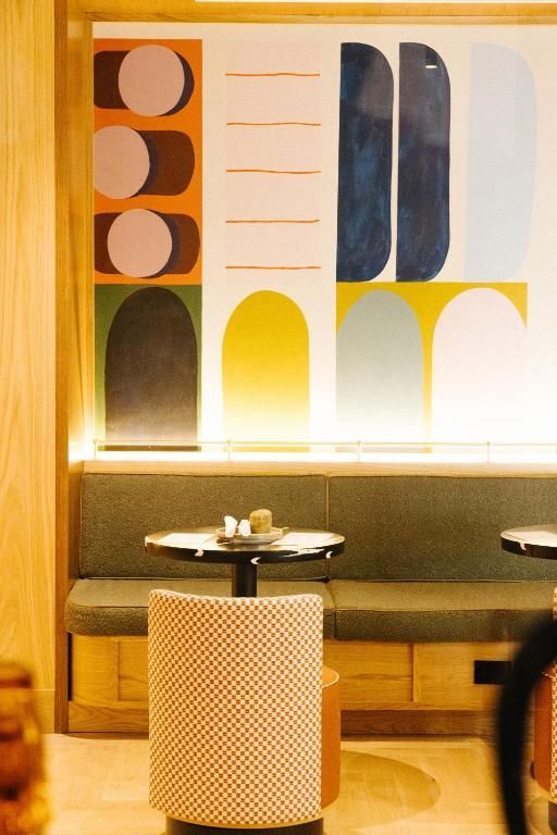 Een sfeervol café-interieur met kleurrijke abstracte muurkunst, zitjes en kleine ronde tafels.
