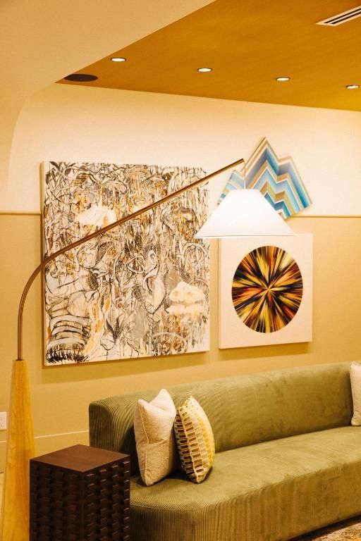 Moderne woonkamer met olijfgroene bank, decoratieve wandbekleding, witte hanglamp en warmgeel plafond.