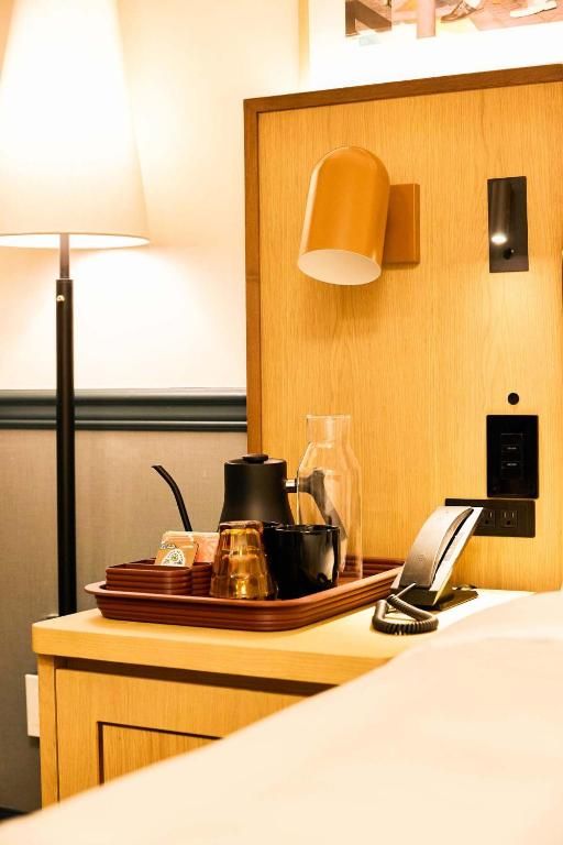 Hotelnachtkastje met lamp, theeservies en telefoon tegen een houten hoofdeinde.