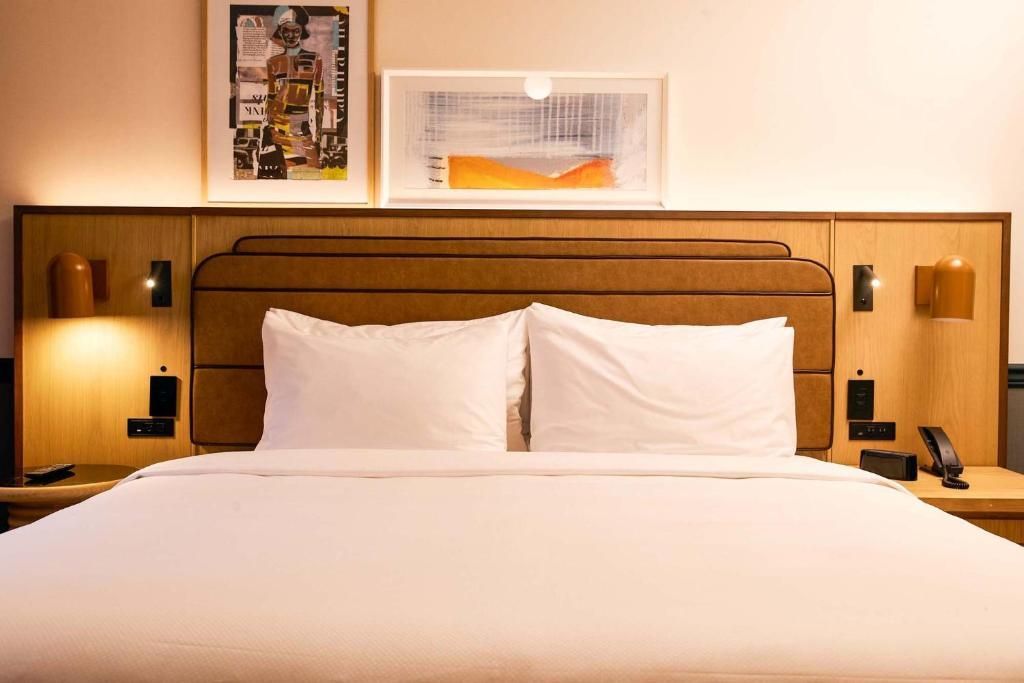 Moderne hotelkamer met een netjes opgemaakt bed, sfeervolle nachtlampjes en ingelijste kunstwerken aan de muur.