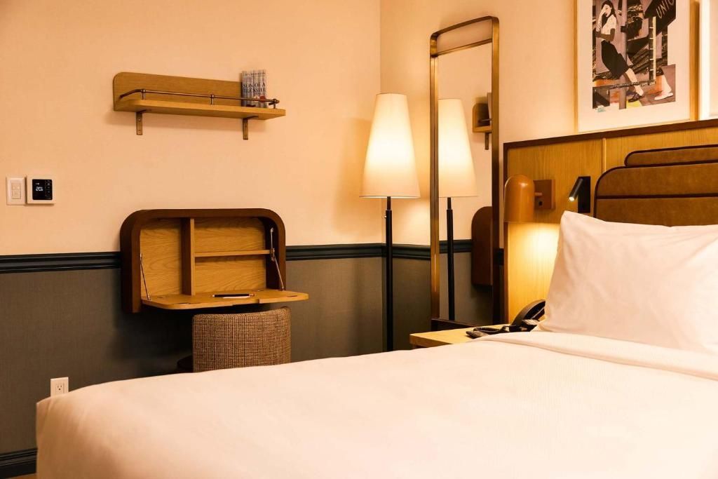 Moderne hotelkamer met opgemaakt bed, wandplank, spiegel en sfeervolle lampverlichting.