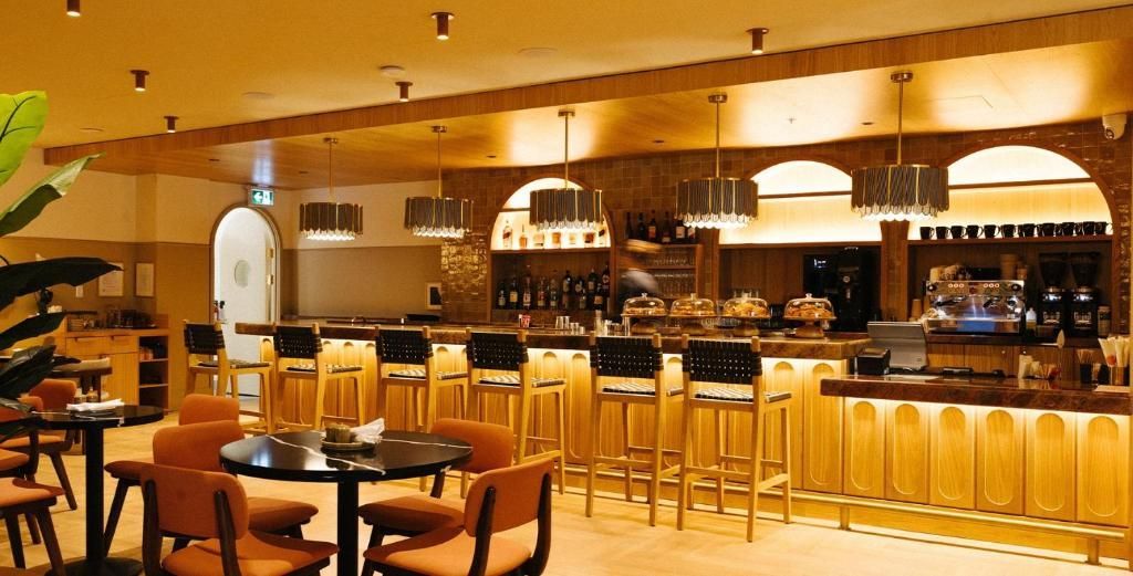 Een lege restaurantbar met houten barkrukken, warme verlichting en netjes gedekte tafels op de voorgrond.
